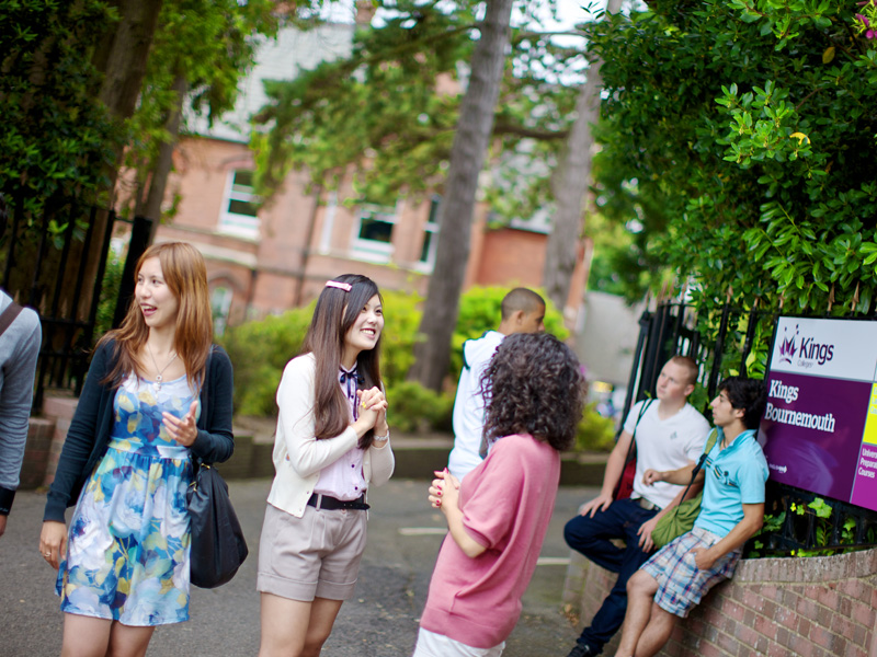 Internationale Schüler unterhalten sich fröhlich vor dem Eingang der Kings Sprachschule Bournemouth.