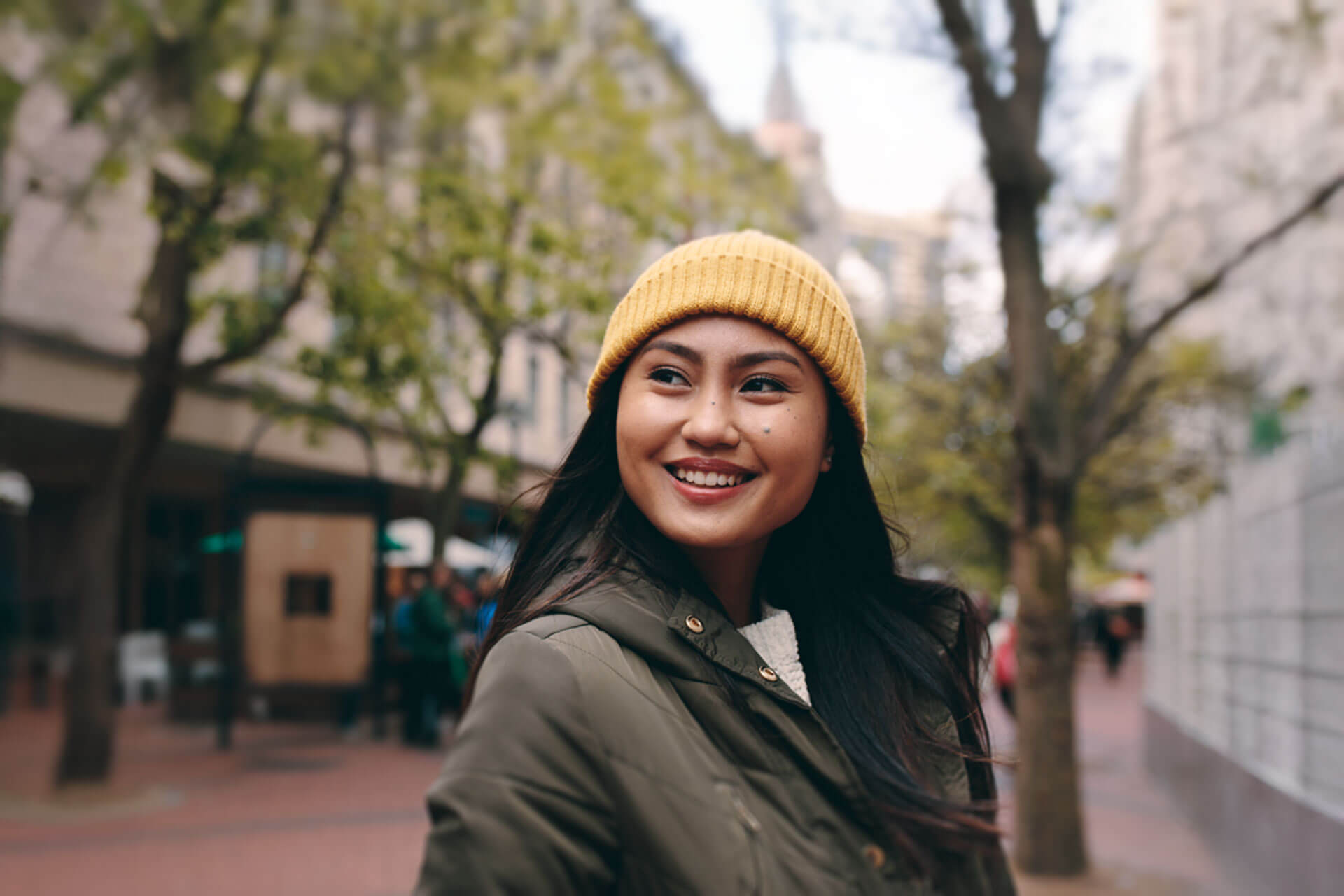 Junge Frau mit gelber Mütze lächelt fröhlich in einer Straße in Brighton während ihres Sprachaufenthalts in England.