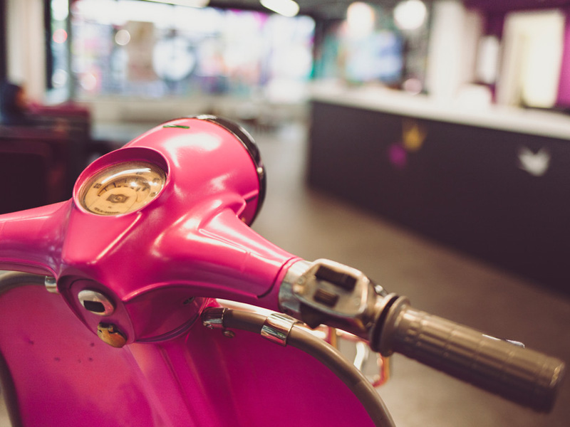 Detailaufnahme eines pinkfarbenen Motorrollers im Eingangsbereich der Schule