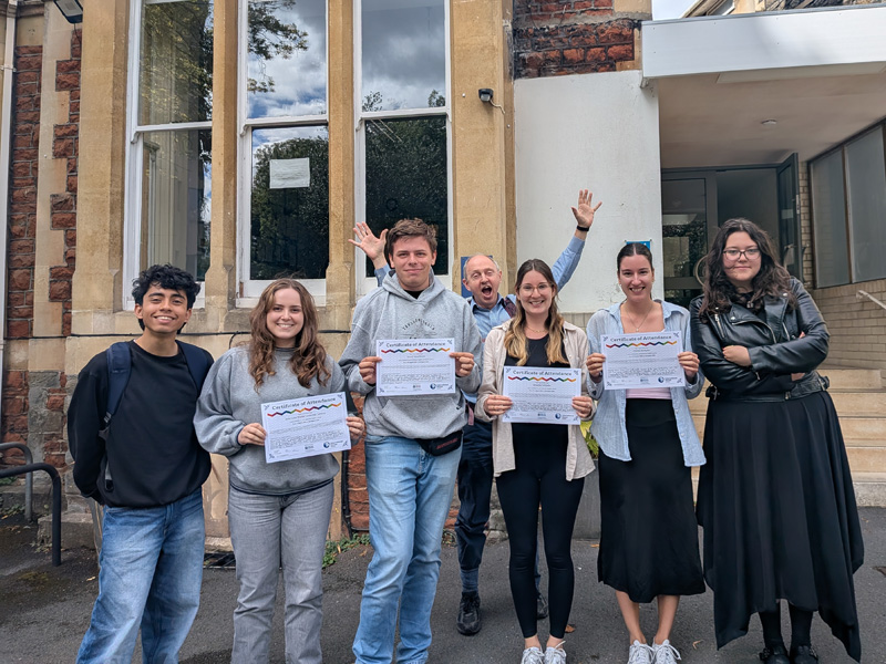 Teilnehmende mit Zertifikaten vor dem Gebäude der IH Bristol Sprachschule nach Kursabschluss