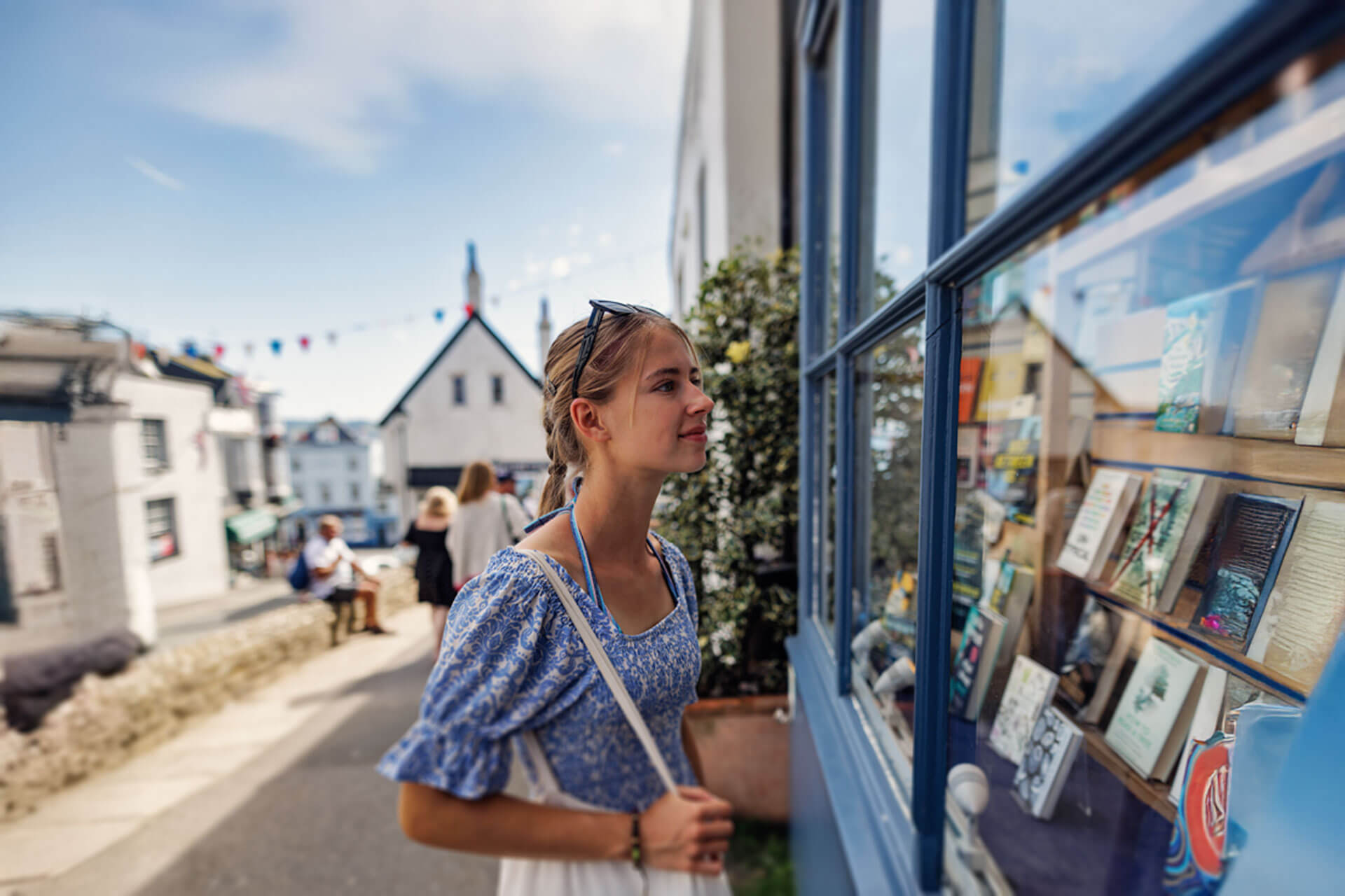 Junge Person betrachtet Schaufenster mit Büchern in einer sonnigen Gasse eines englischen Küstenorts