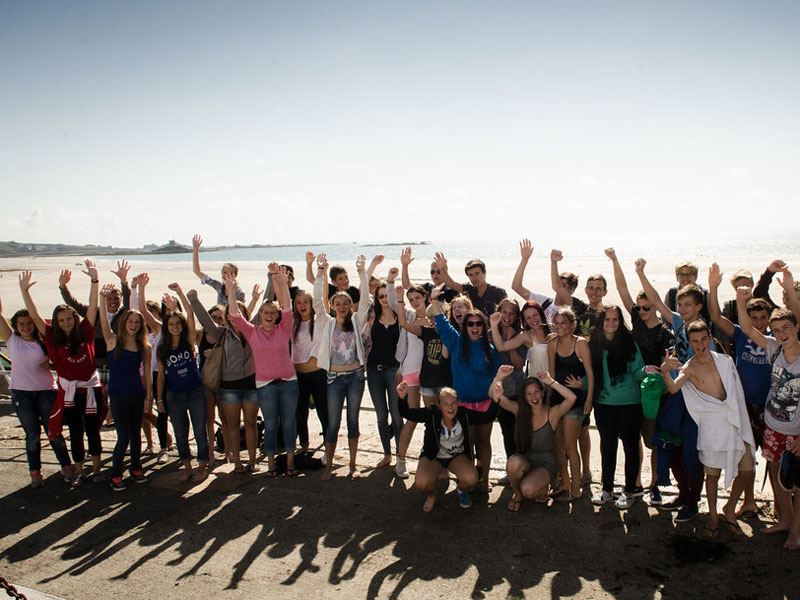 Große Schülergruppe posiert fröhlich am Strand während des Sprachcamps auf Jersey
