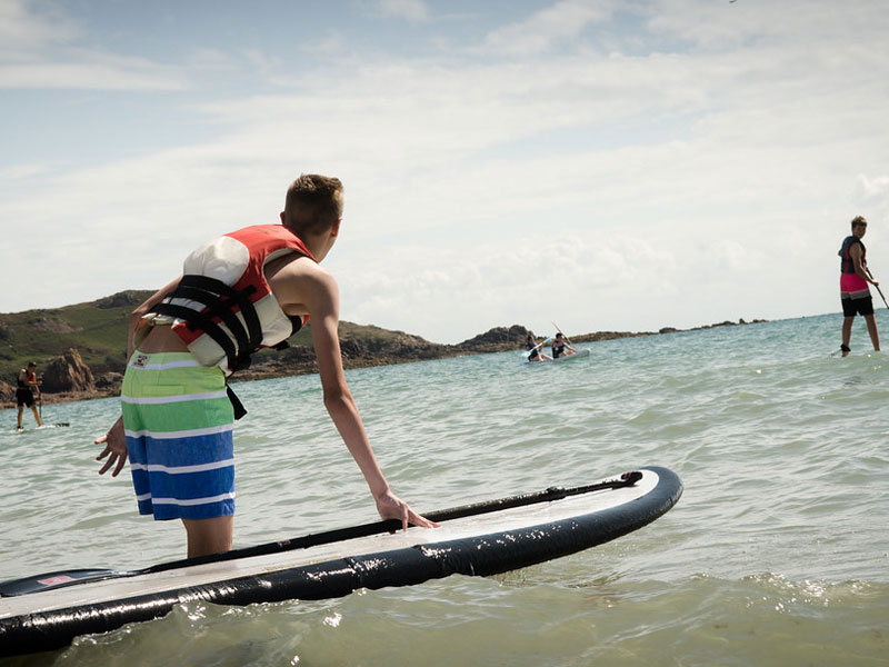 Teilnehmende der Sprachreise probieren Stand-up-Paddling im Meer vor Jersey