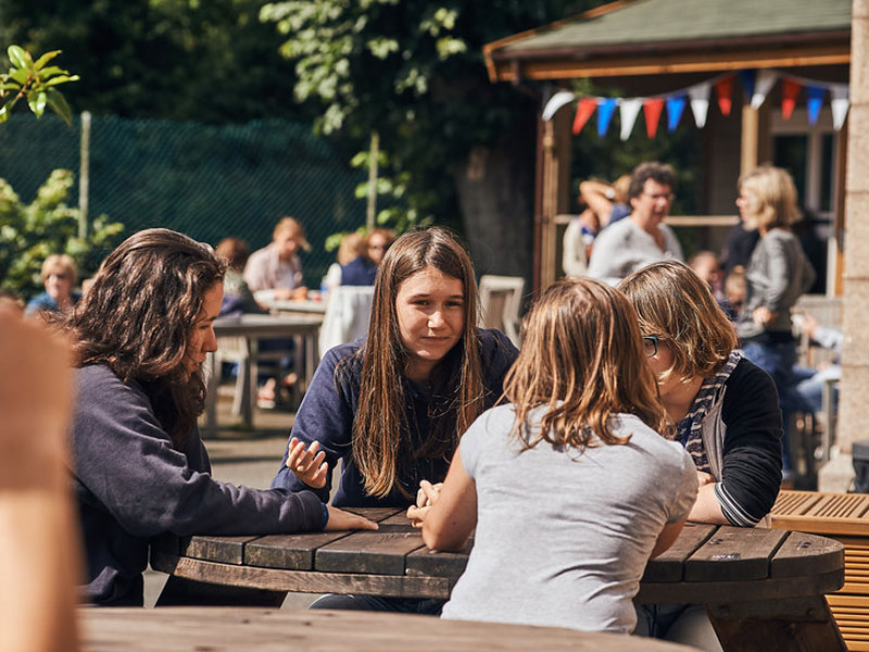 Jugendliche unterhalten sich an Holztischen im Garten der Sprachschule auf Jersey