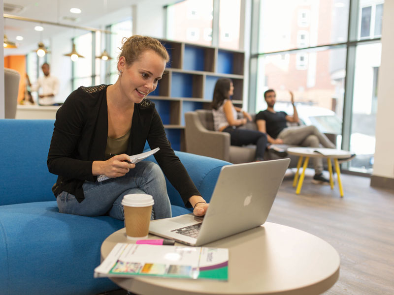 Teilnehmerin arbeitet mit Laptop und Unterlagen in der hellen Lounge der Kaplan Sprachschule Liverpool