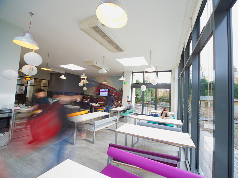 Moderne Cafeteria mit großen Fenstern und bunten Sitzbänken an der Kings London Beckenham