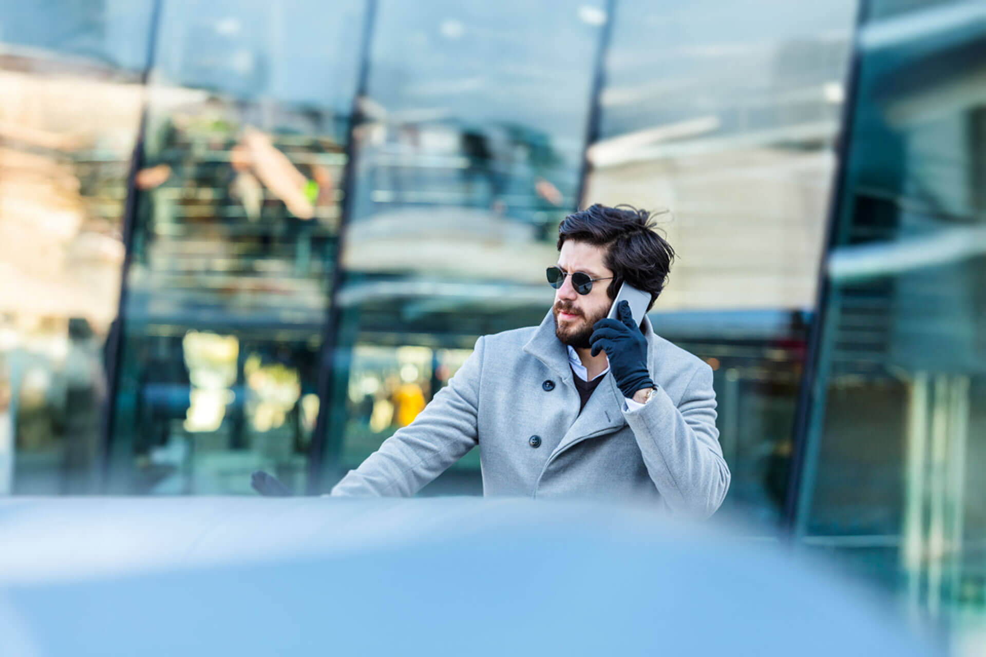 Person mit Mantel und Sonnenbrille telefoniert vor einem modernen Glasgebäude in London