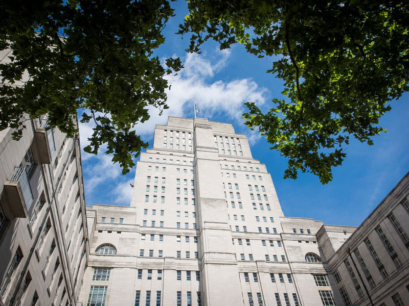 Hauptgebäude der LSE in London mit blauem Himmel und grünen Baumkronen im Vordergrund