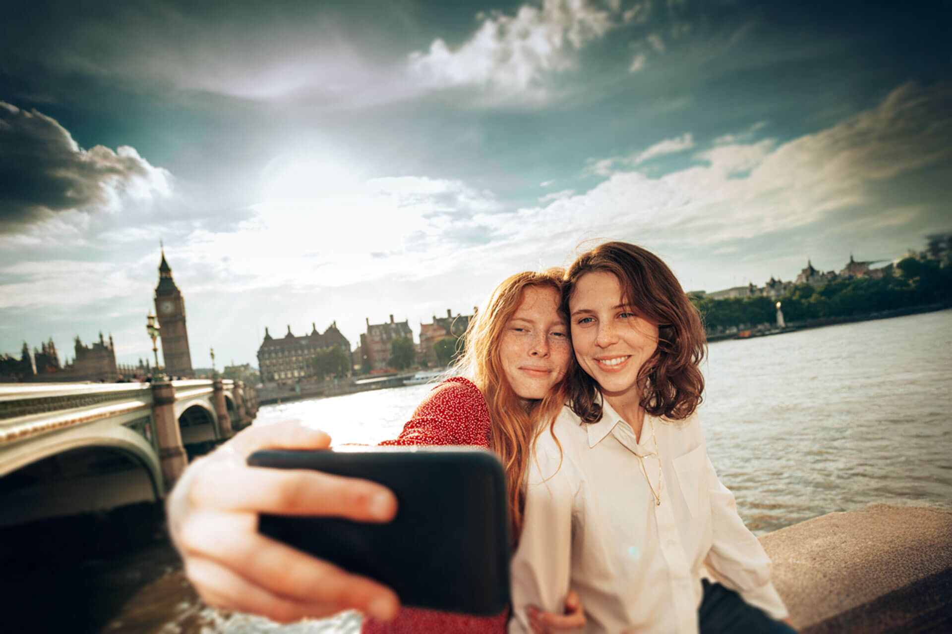 Zwei Personen machen ein Selfie an der Themse mit Blick auf die Westminster Bridge und den Big Ben in London
