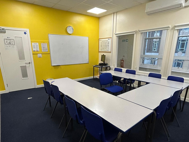 Unterrichtsraum der International House Newcastle mit gelber Wand und Whiteboard