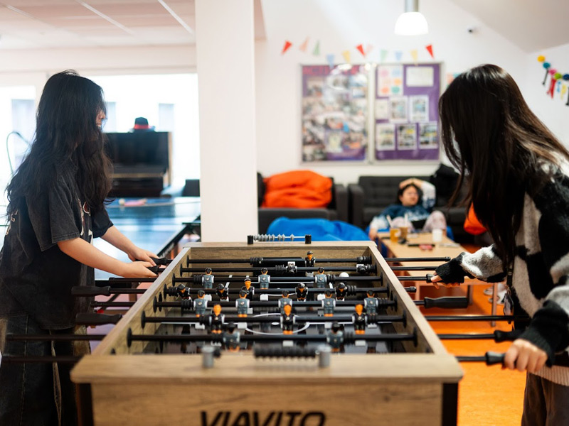Teilnehmende spielen Tischfußball und üben Englisch im Freizeitbereich der Sprachschule