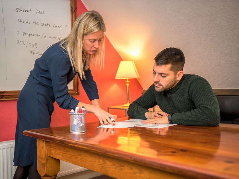 Lehrkraft erklärt einem Lernenden eine Aufgabe im Klassenraum.