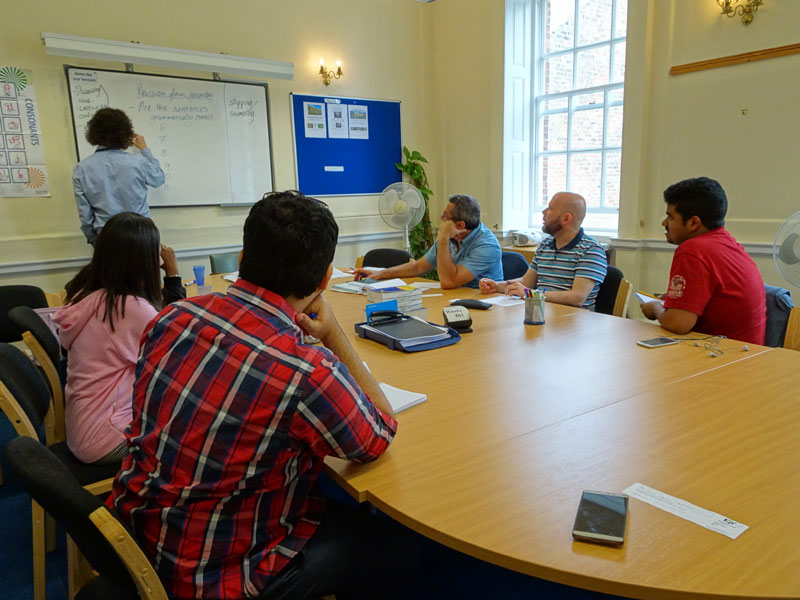Lehrkraft schreibt an die Tafel, während Sprachschüler:innen aufmerksam am Unterricht teilnehmen