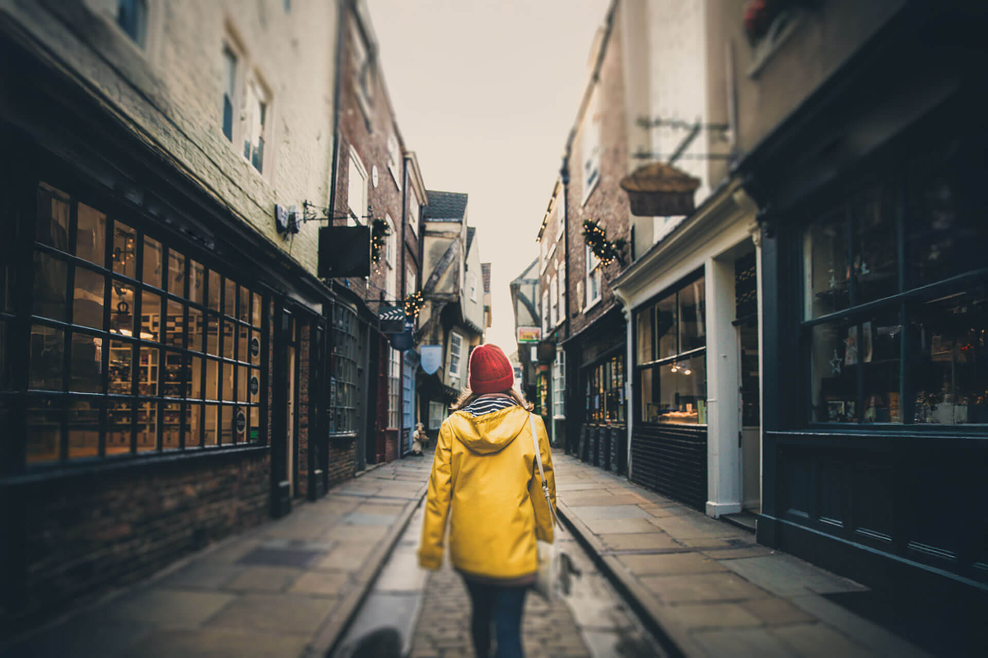 Person mit gelber Jacke und roter Mütze spaziert durch eine enge, historische Gasse in York