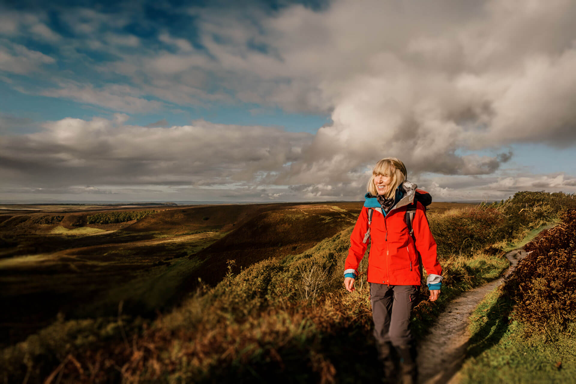Person mit roter Jacke wandert durch die hügelige Landschaft der North York Moors bei wechselhaftem Wetter