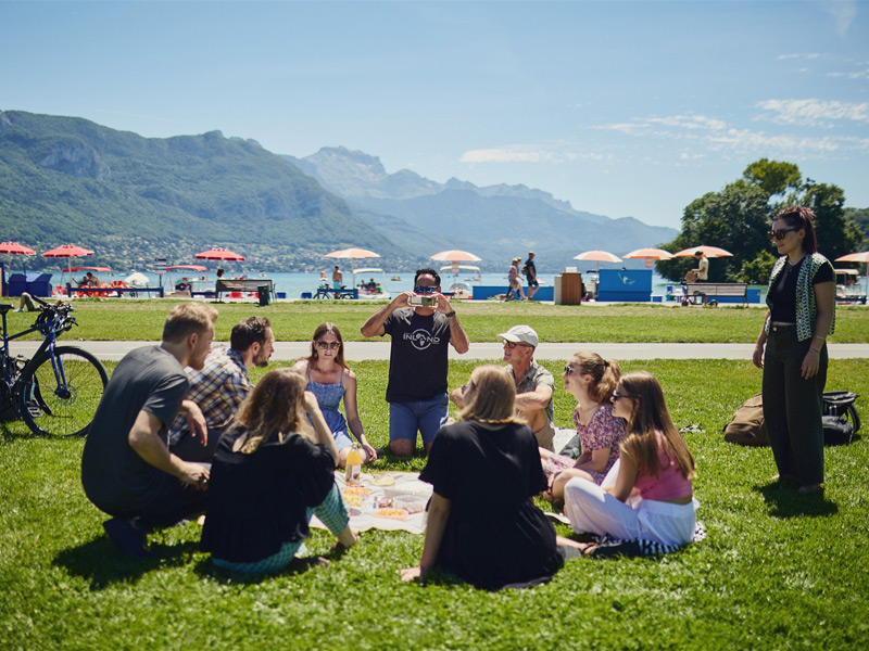 Sprachschüler geniessen ein Picknick am See von Annecy mit Blick auf die Alpen