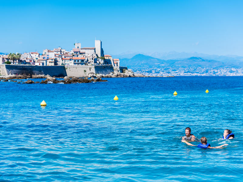 Jugendliche baden im Mittelmeer mit Blick auf die Altstadt von Antibes