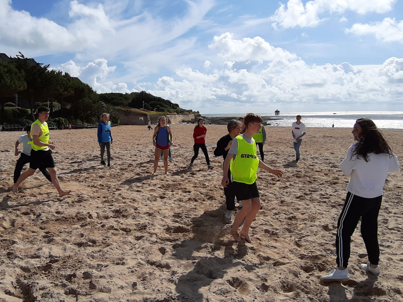 Schülerinnen und Schüler spielen gemeinsam Beachvolleyball am Strand von La Rochelle