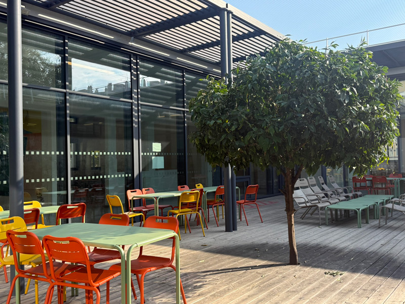 Sonniger Innenhof des Eucalyptus Campus in Nizza mit farbigen Tischen und Stühlen