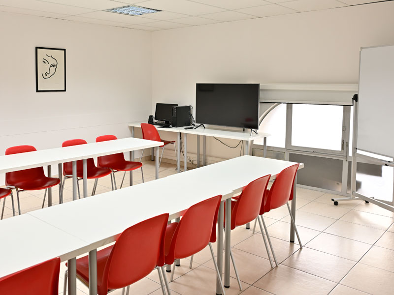 Salle de classe lumineuse de l'école de français à Nice avec tables, chaises rouges et écran numérique.