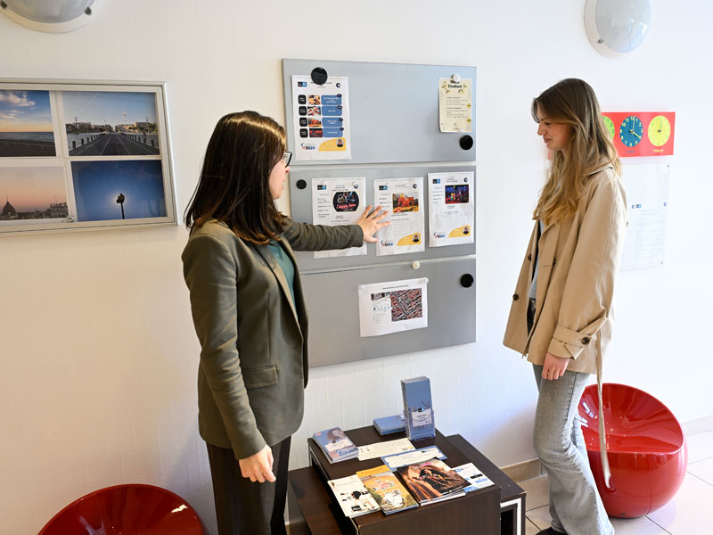 Une employée de l'école de langues à Nice explique les activités et les informations affichées sur le tableau d'information.
