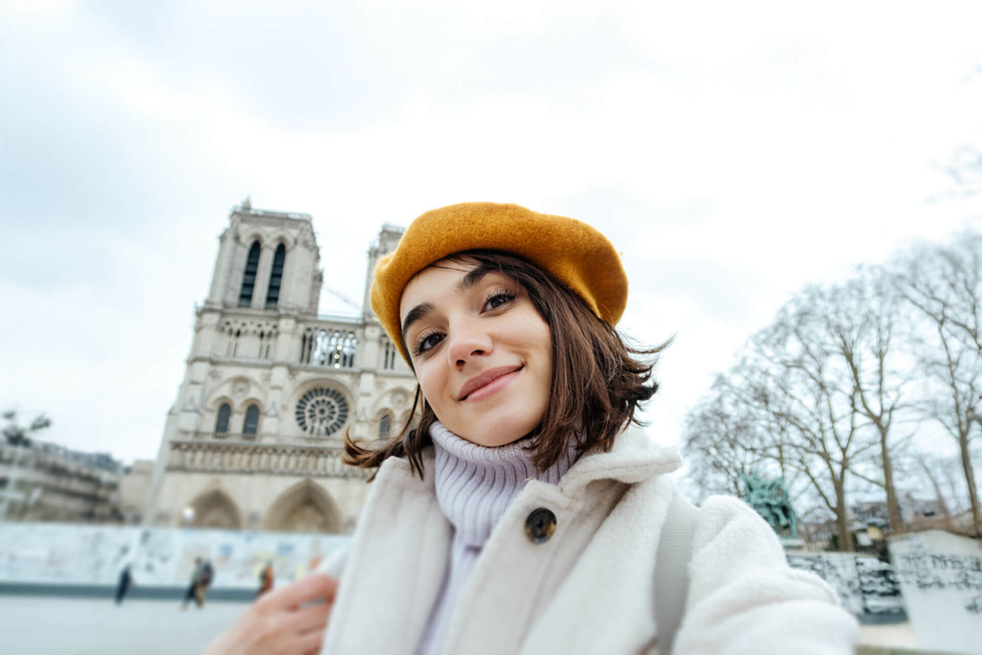 Junge Frau mit Baskenmütze vor der Kathedrale Notre-Dame in Paris während ihres Sprachaufenthalts in Frankreich