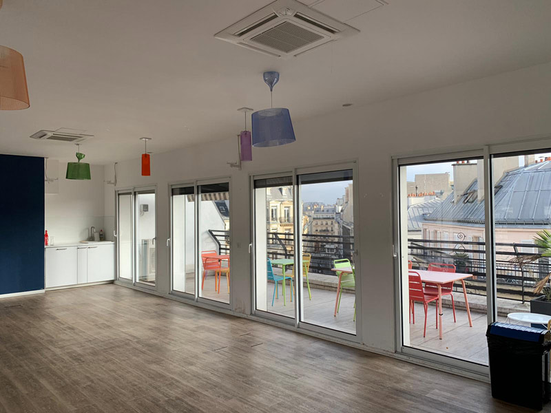 Aufenthaltsraum der Les Ateliers FL Sprachschule Paris mit Zugang zur Terrasse und weitem Stadtblick