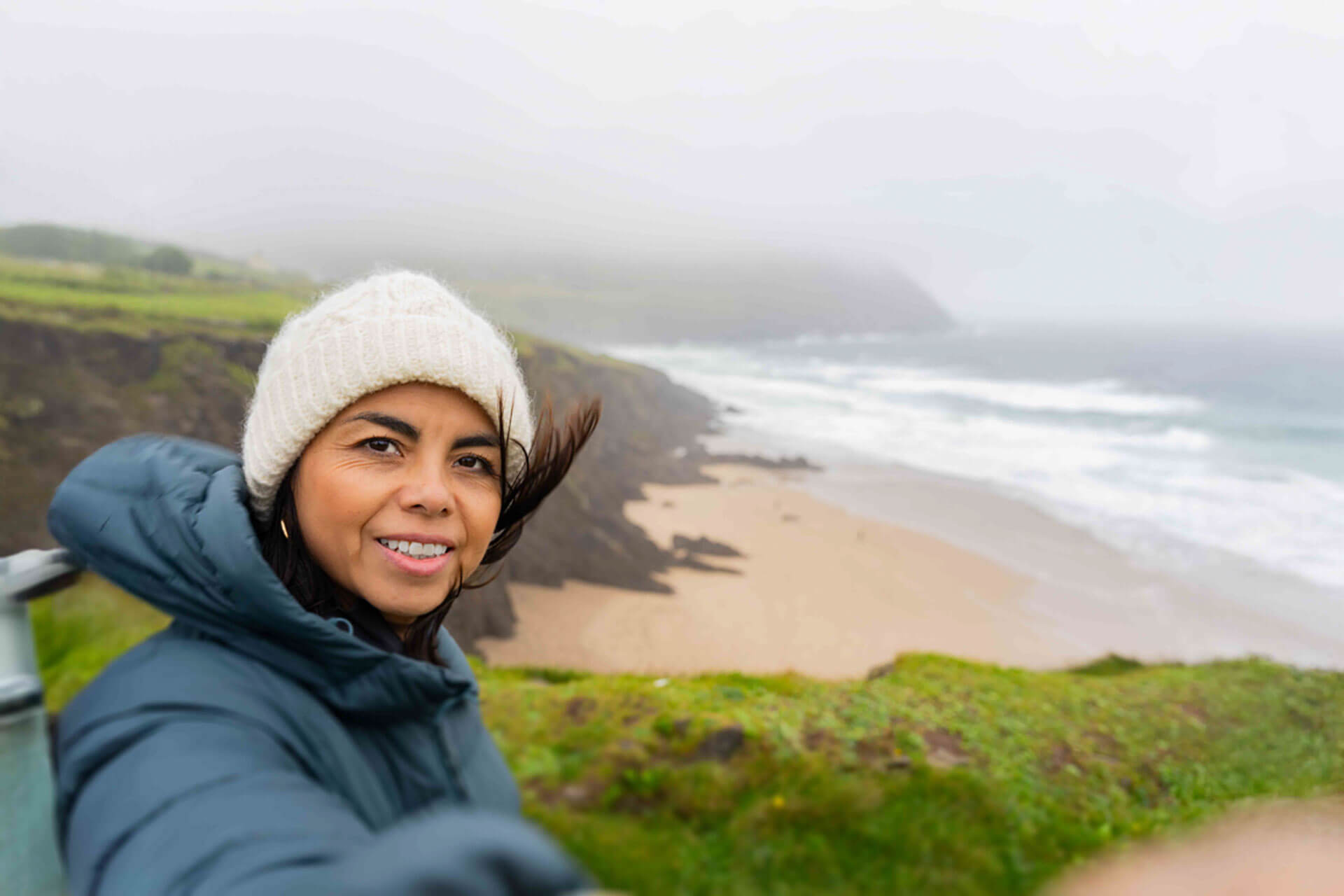 Person macht ein Selfie an der windigen Küste Irlands mit Blick auf Meer und Klippen