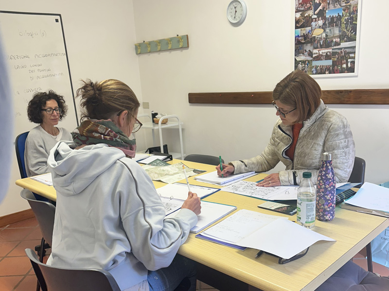 Lehrkraft unterrichtet Kleingruppe an der Scuola Palazzo Malvisi mit Lernunterlagen