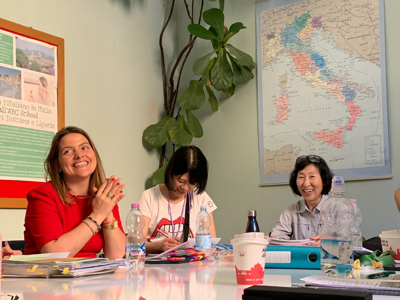 Lehrkraft unterrichtet kleine internationale Gruppe im hellen Klassenraum mit Italienkarte