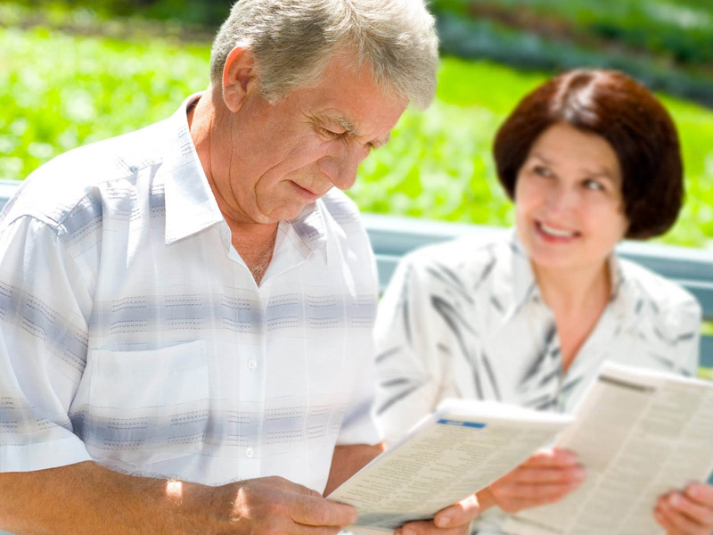 Älteres Paar sitzt im Park und liest gemeinsam, während sie sich unterhalten