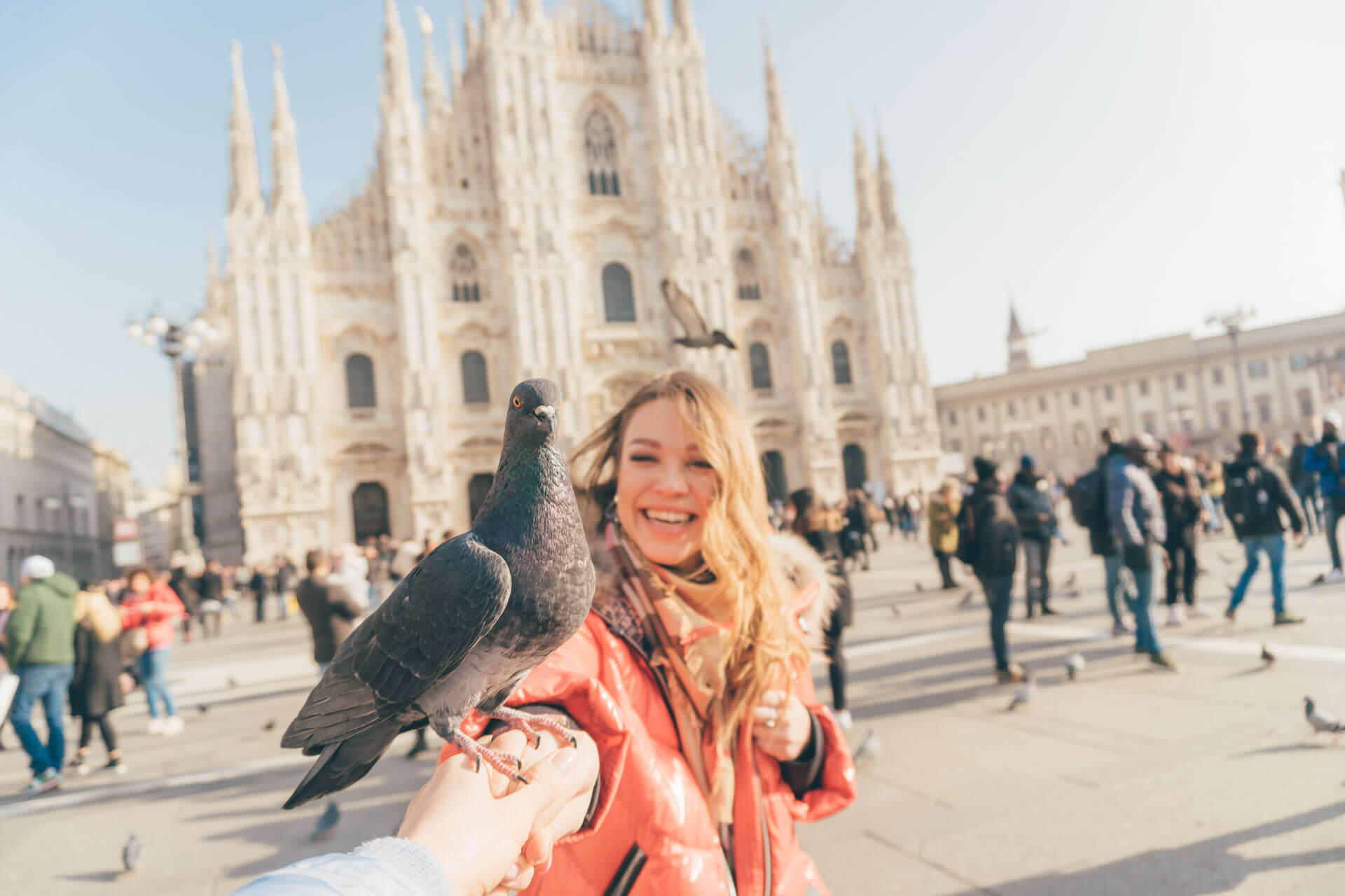 Junge Frau füttert Tauben auf dem Domplatz in Mailand vor der beeindruckenden Fassade des Mailänder Doms