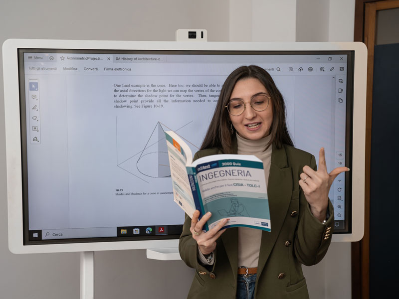 Docente nel corso di italiano a Milano con libro davanti a schermo digitale nella scuola di lingua