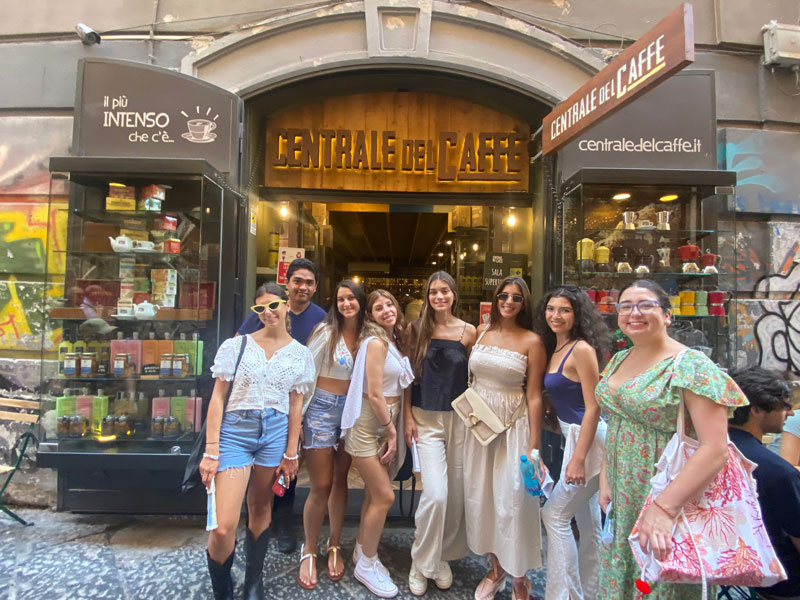 Gruppe junger Erwachsener posiert lachend vor einem Café im Zentrum von Neapel