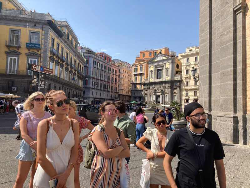 Teilnehmende einer Stadtführung entdecken historische Gebäude im sonnigen Neapel