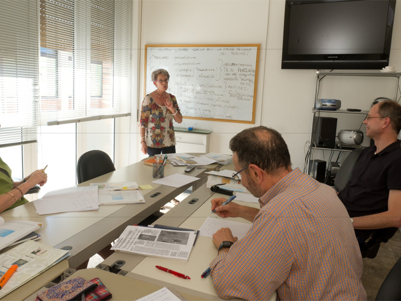 Lehrerin steht an der Tafel und erklärt grammatikalische Inhalte einer kleinen Lerngruppe