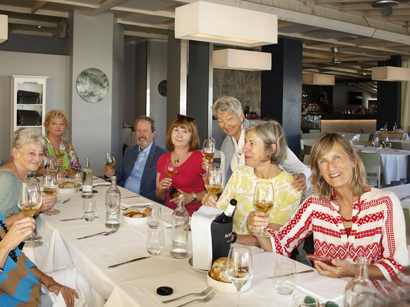 Gruppe älterer Erwachsener sitzt in einem Restaurant und stößt mit Weißwein an