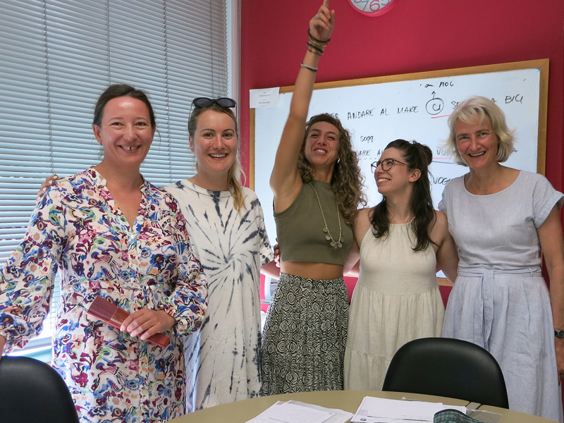 Fünf Kursteilnehmerinnen lächeln in einem Klassenzimmer vor einer beschrifteten Tafel