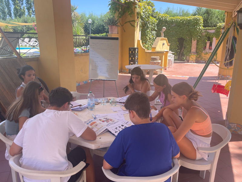 Sprachschüler lernen im Freien an einem Tisch unter einer überdachten Terrasse