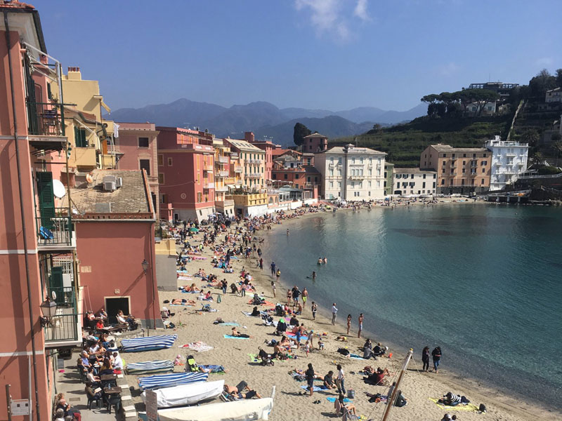 Blick auf den belebten Strand und die bunten Häuser der Baia del Silenzio in Sestri Levante