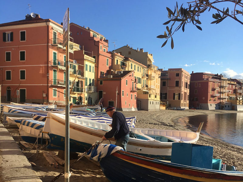 Fischer kümmert sich um sein Boot am Strand von Sestri Levante vor bunten Häusern