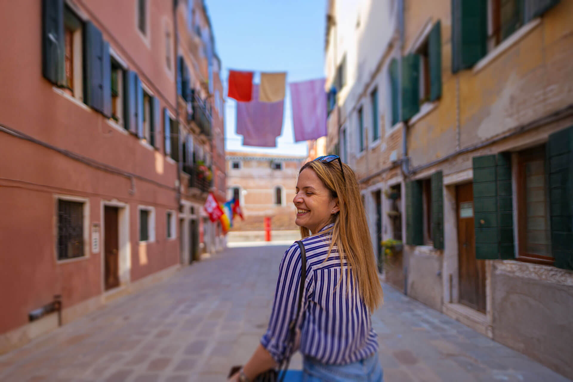 Junge Frau spaziert lächelnd durch eine malerische Gasse in Sestri Levante mit bunten Häusern und Wäscheleinen über der Straße