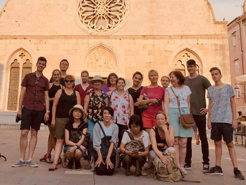 Gruppe von Sprachschüler:innen steht vor einer historischen Kirche in Triest und posiert für ein Gruppenfoto