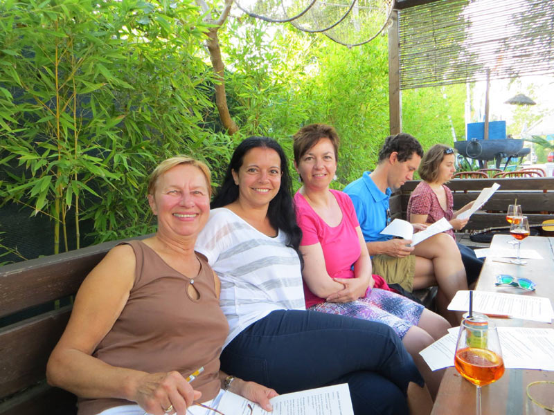 Sprachschüler:innen sitzen entspannt im Gartenlokal und unterhalten sich bei Getränken