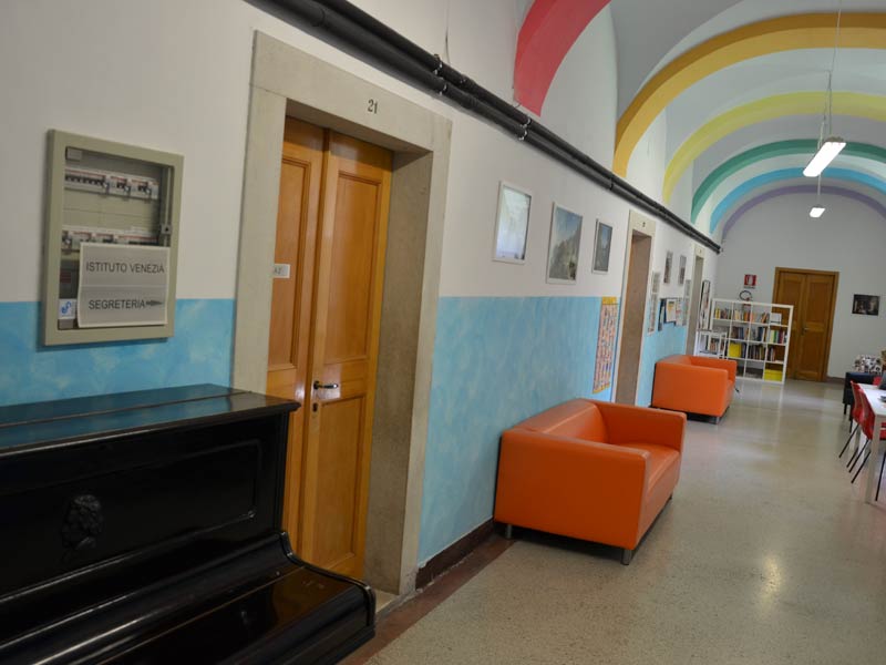 Flur der Piccola Università Italiana Triest mit bunten Deckenbögen, orangefarbenen Sofas und Wanddekoration