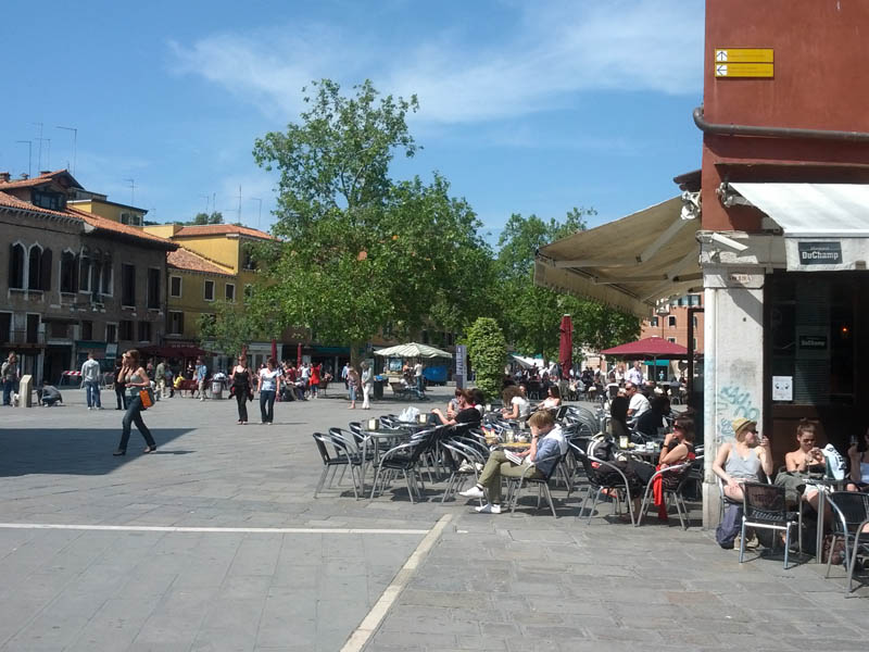 Menschen genießen die Sonne in einem Straßencafé auf einem Platz nahe des Istituto Venezia