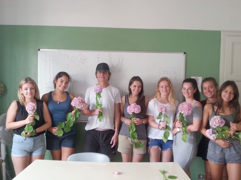 Sprachschüler halten Blumen in den Händen und posieren gemeinsam im Klassenraum der Sprachschule