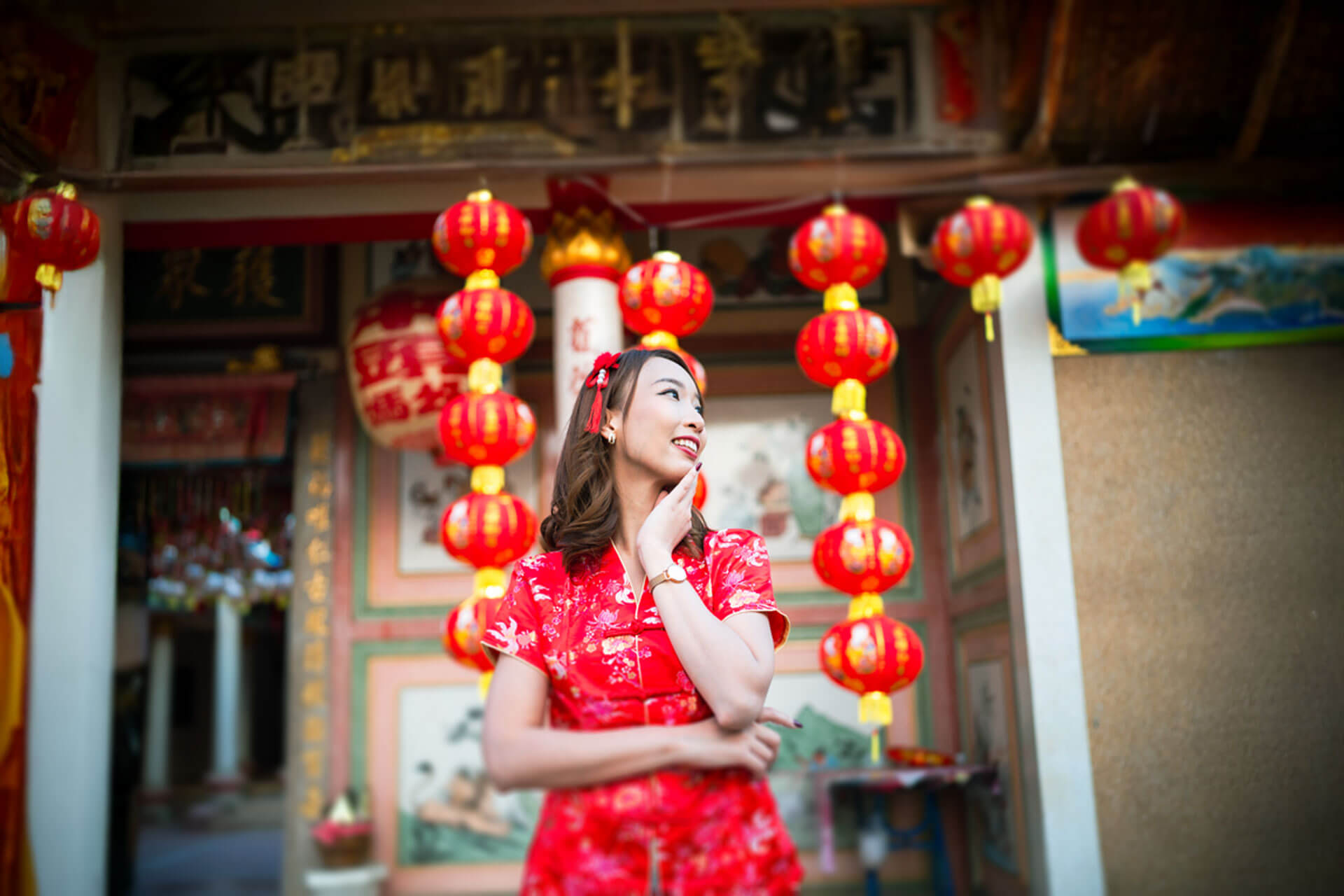 Person in traditioneller roter Kleidung steht vor einem Tempel mit roten Laternen in Kyoto