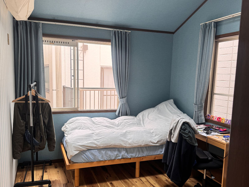 Helles Schlafzimmer in einer japanischen Gastfamilie in Tokio mit Einzelbett, Schreibtisch und großen Fenstern.