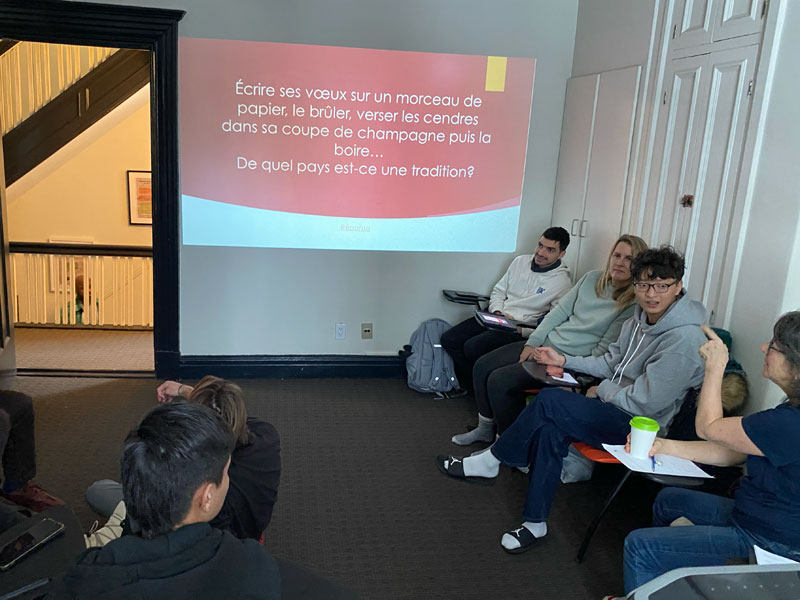 Gruppe von Sprachschülern diskutiert vor einer Wandprojektion mit französischem Text